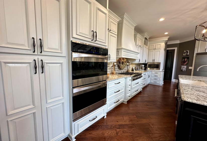 Kitchen with stainless steel appliances, light stone counters, white cabinetry, dark wood-style floors, and hanging light fixtures