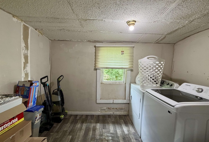 Laundry area with wood-finish flooring, a single window with blinds, and ceiling-mounted light fixture