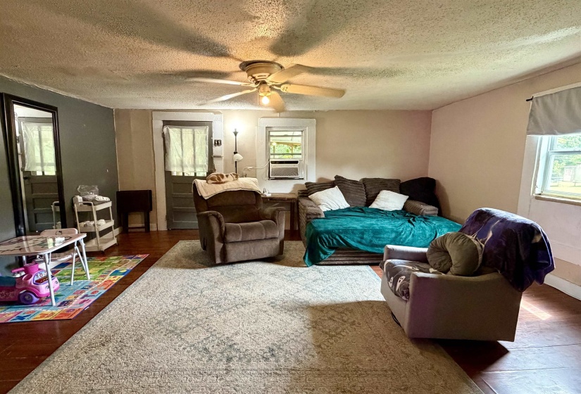 Spacious living area featuring wood-finish flooring, a ceiling fan with integrated lighting, and multiple windows providing natural illumination