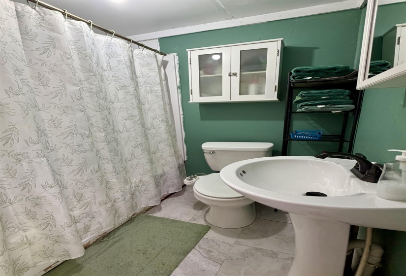 Bathroom featuring a white pedestal sink with a dark-finish faucet, a white toilet, and light-toned floor tile