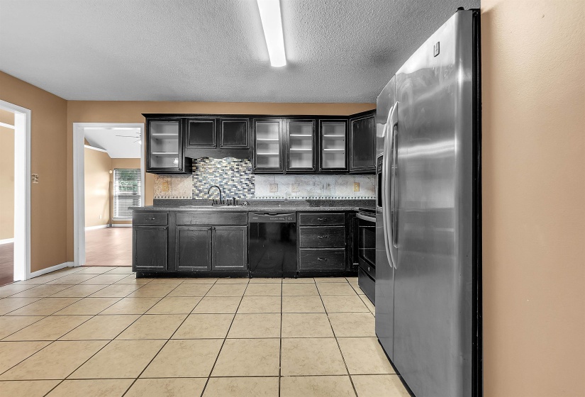 Kitchen featuring tile flooring, dark cabinetry, a patterned tile backsplash, and a stainless steel refrigerator