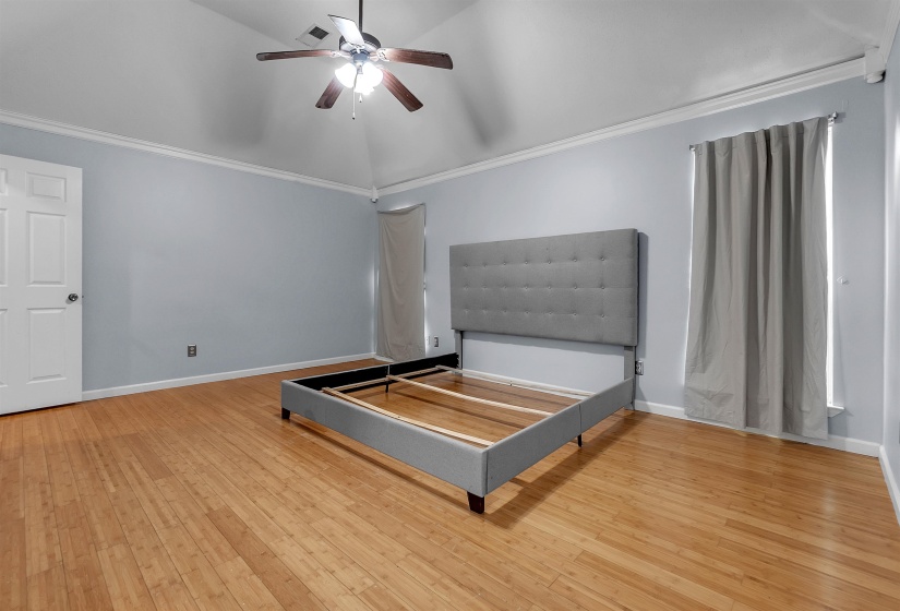 Vaulted ceiling bedroom with wood-finish flooring, ceiling fan, crown molding, and light-toned walls