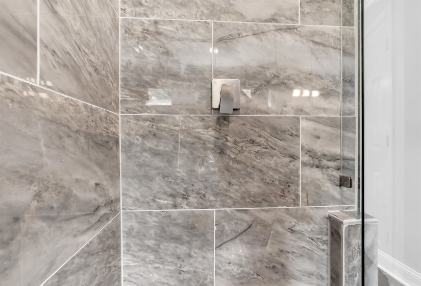 Shower enclosure featuring large format gray marble-look wall tiles, a brushed nickel shower control, and a clear glass door with a complementary handle