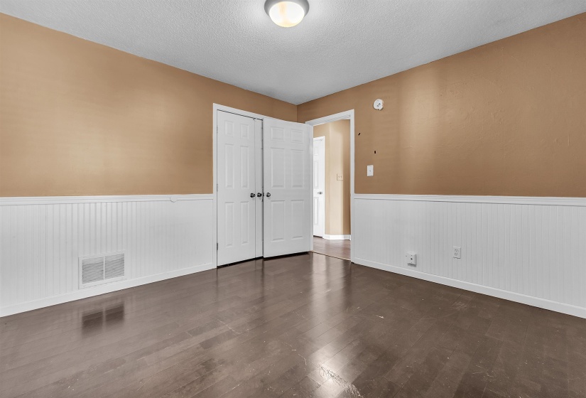 Interior room featuring dark wood-finish flooring, white beadboard wainscoting, and neutral tan walls