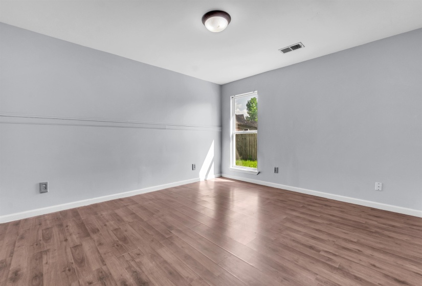 Spacious room featuring wood-finish flooring, light gray walls, white baseboards, and a single window