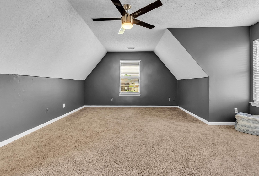 Spacious room featuring vaulted ceilings, a ceiling fan with integrated lighting, and two windows with blinds