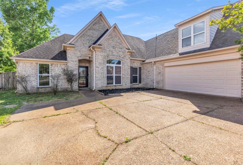 Light brick exterior featuring a multi-gabled roofline, an arched entryway with security door, and a two-car garage with overhead dormer