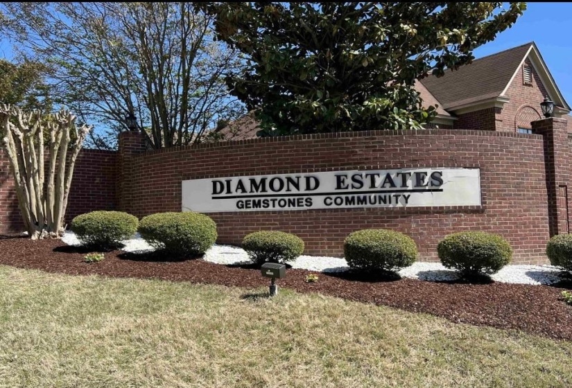 Brick entrance wall featuring a large community sign, manicured shrubs, white decorative stone, and fresh mulch