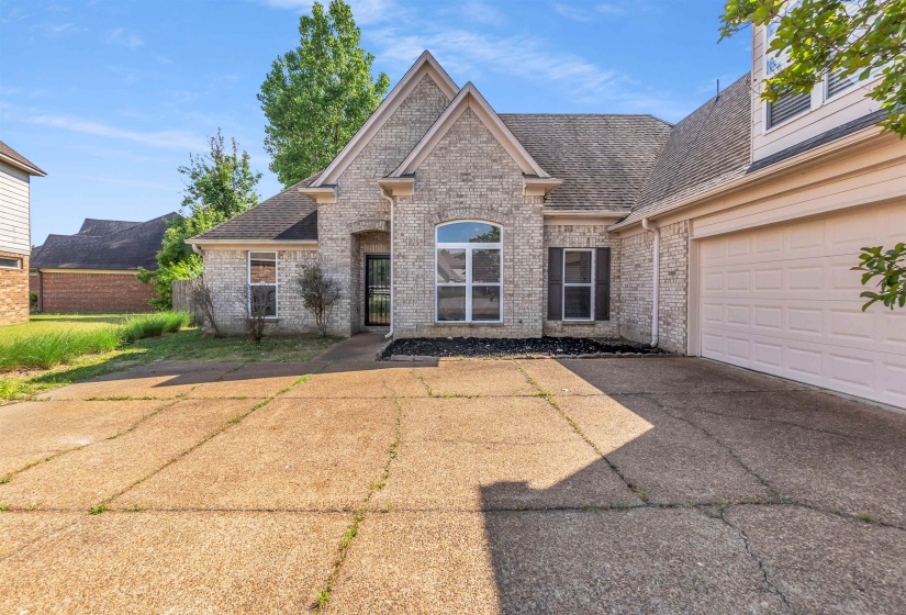 Brick exterior featuring an arched window, dark shutters, and an attached two-car garage