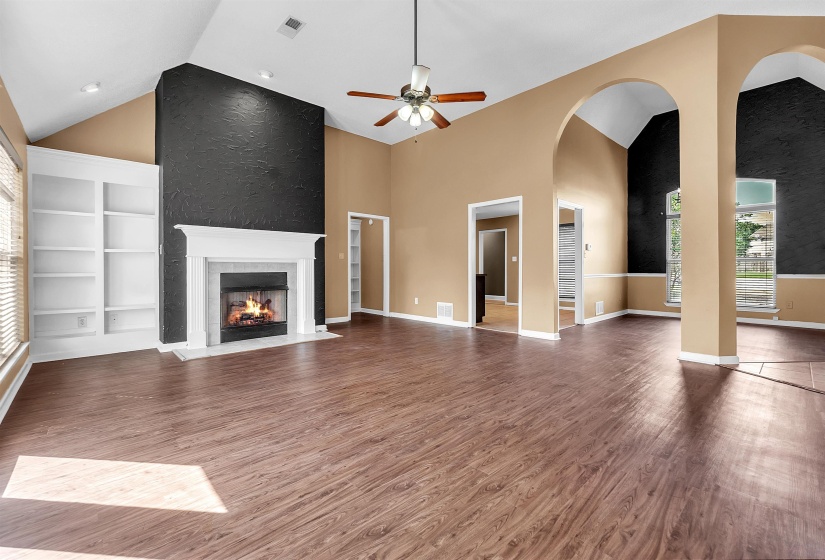 Spacious living area featuring high vaulted ceilings, wood-finish flooring, a fireplace with a white mantel, built-in shelving, and a ceiling fan