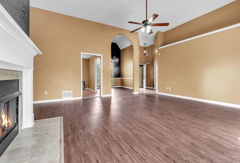 Spacious living area featuring wood-finish flooring, a fireplace with a white mantel and tile surround, a ceiling fan, arched doorways, and vaulted ceilings