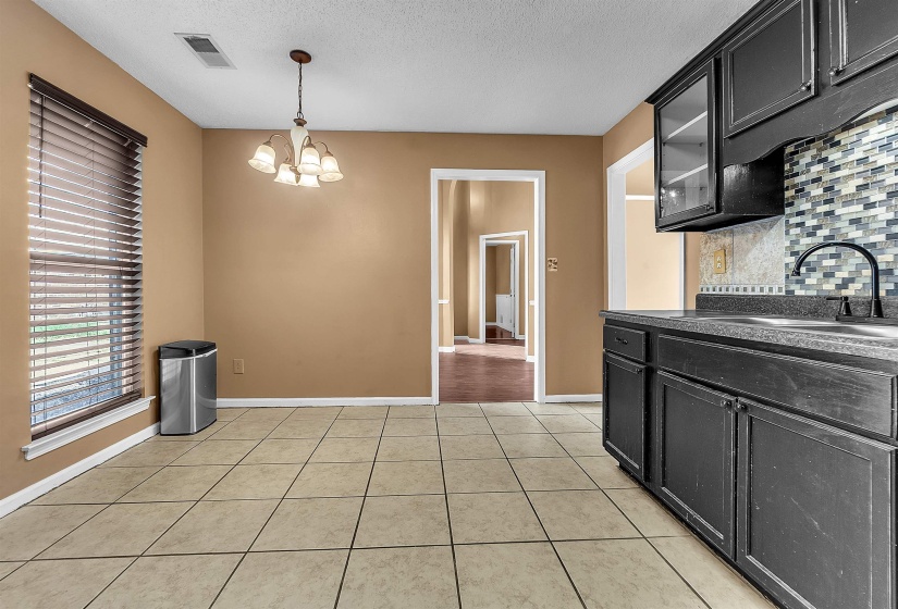 Open-concept dining area featuring tiled flooring, a multi-light chandelier, and a window with horizontal blinds