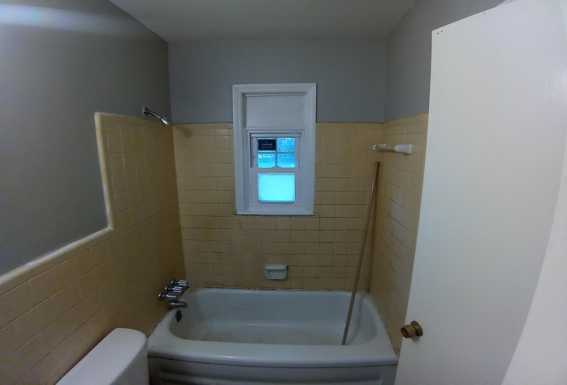 Bathroom featuring tiled shower / bath, toilet, and tile walls
