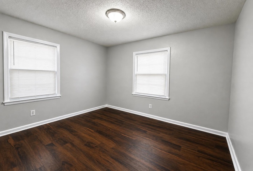 Room featuring two windows with blinds, wood-finish flooring, light gray walls, white baseboards, and a semi-flush ceiling light fixture