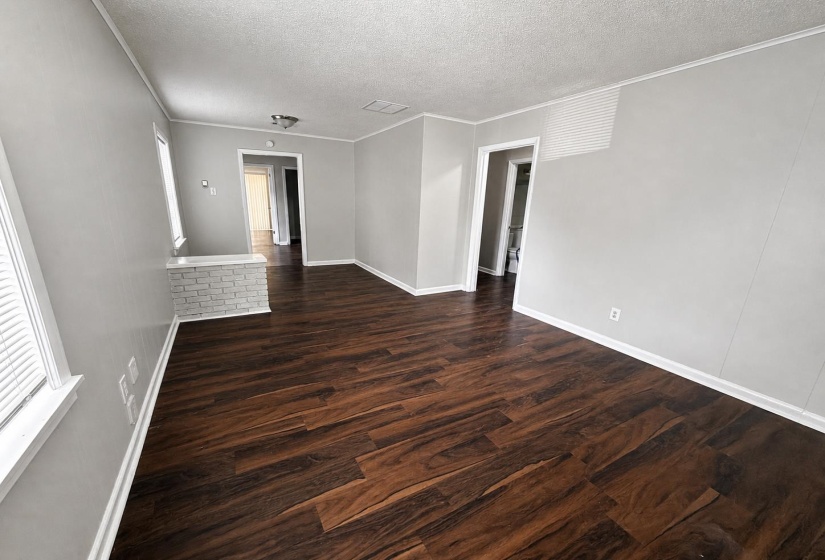 Spacious room featuring wood-finish flooring, light gray wall paint, white baseboards, and a white brick half-wall
