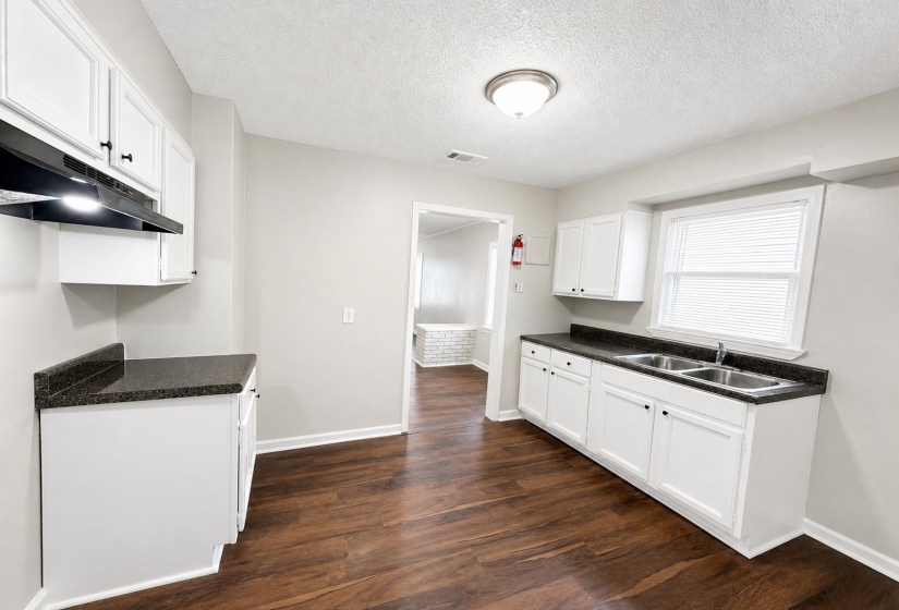 Kitchen featuring wood-finish flooring, white cabinetry with dark hardware, dark countertops, and a double-basin sink
