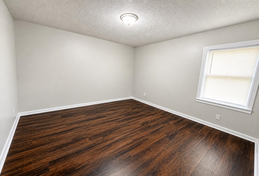 Bright interior room featuring wood-finish flooring, light gray walls, white trim, and a single window with blinds