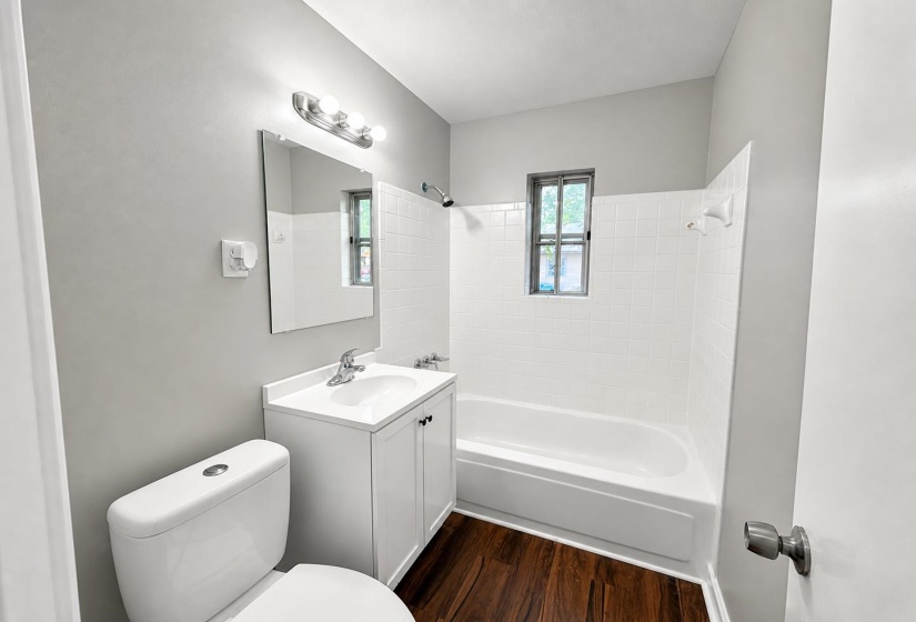 Bathroom with white subway tile shower surround, single vanity with white cabinet, chrome fixtures, and wood-finish flooring