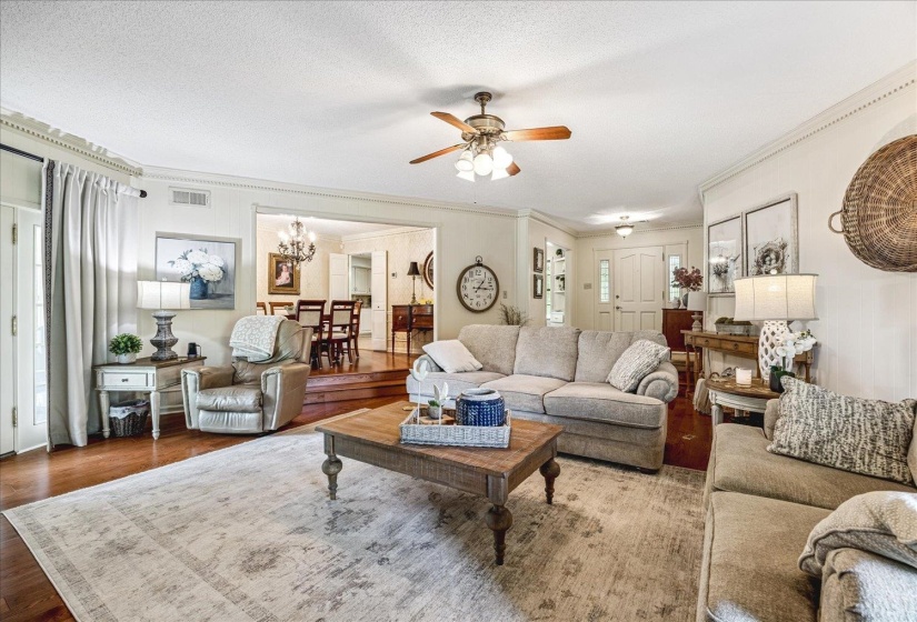 Spacious living area featuring wood-finish flooring, crown molding, a ceiling fan with light fixture, and French doors