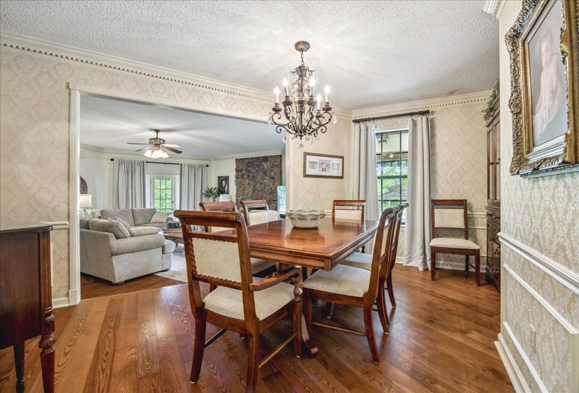 Dining area featuring wood-finish flooring, an ornate chandelier, decorative crown molding, and wainscoting