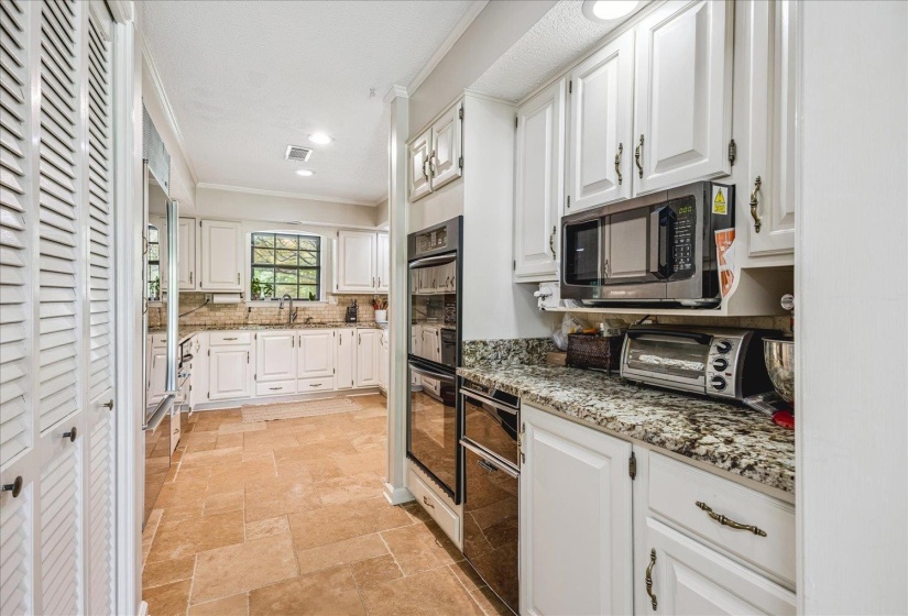 Kitchen featuring white cabinetry, stone tile flooring, built-in double ovens, and granite countertops