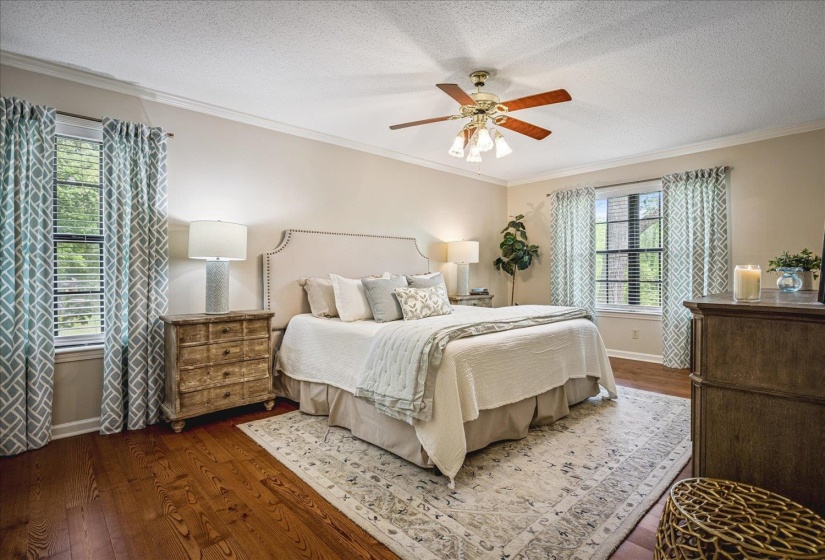 Spacious bedroom featuring wood-finish flooring, crown molding, and two windows with blinds