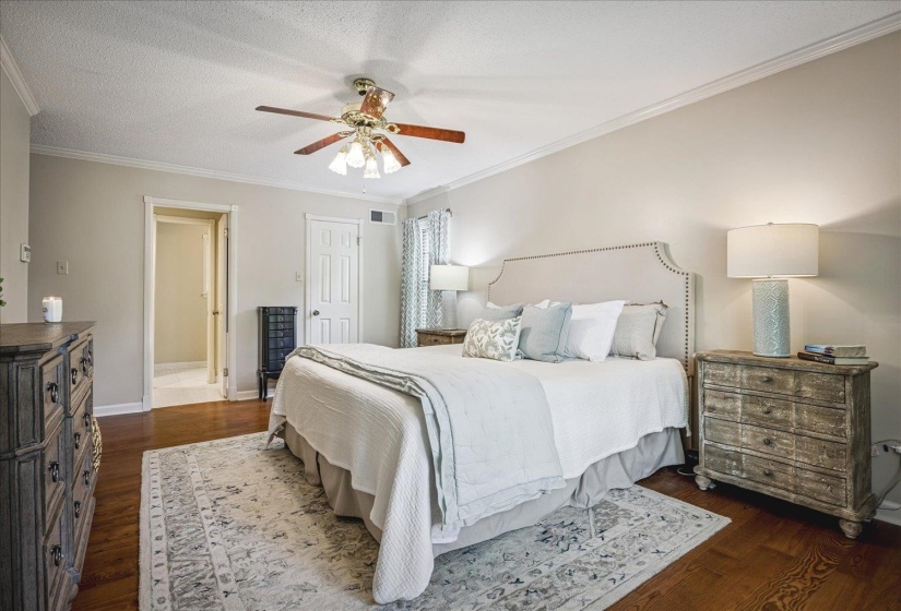 Spacious bedroom featuring wood-finish flooring, a ceiling fan with integrated lighting, crown molding, and neutral wall tones