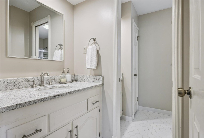 White vanity with brushed nickel hardware, a speckled white countertop, and an undermount sink