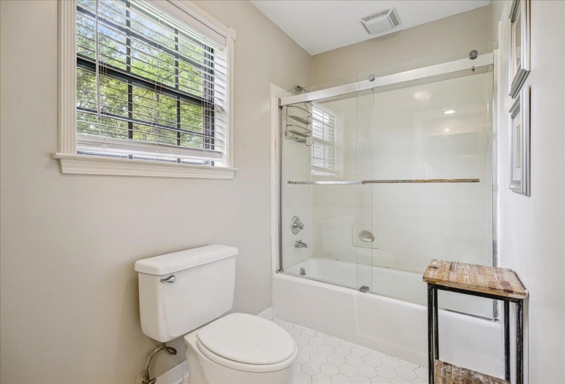 Bathroom featuring a white bathtub with a clear glass sliding door, a white toilet, and hexagonal tile flooring