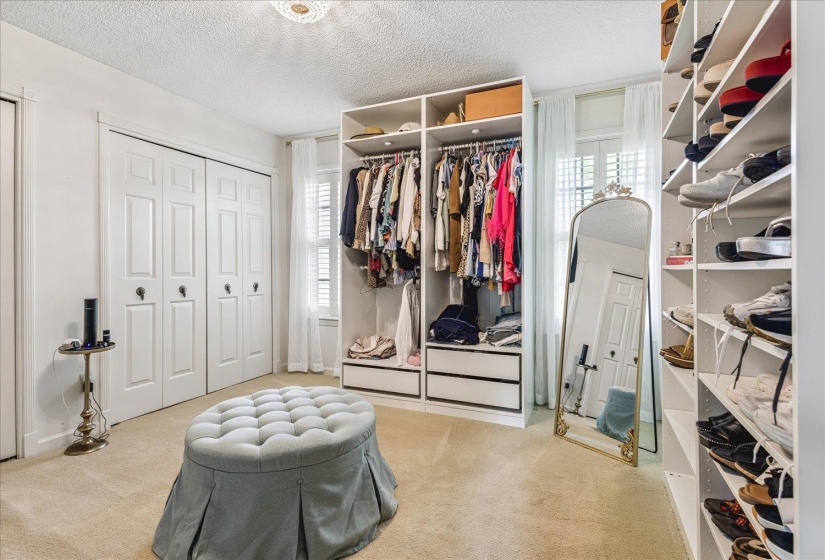 Spacious dressing room featuring custom built-in shelving, ample hanging storage, multiple storage drawers, paneled bi-fold doors, and a decorative ceiling light fixture