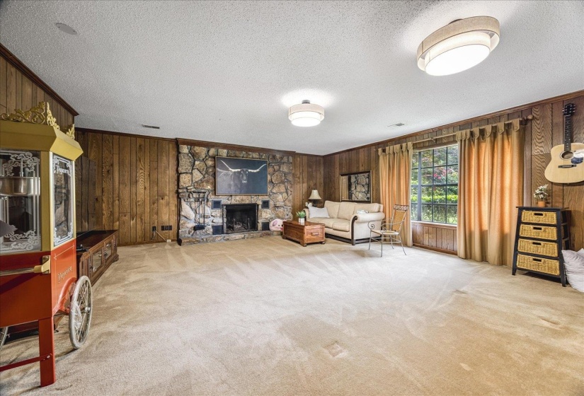 Spacious room featuring wood paneling, a stone-clad fireplace with a hearth, and large window with exterior views