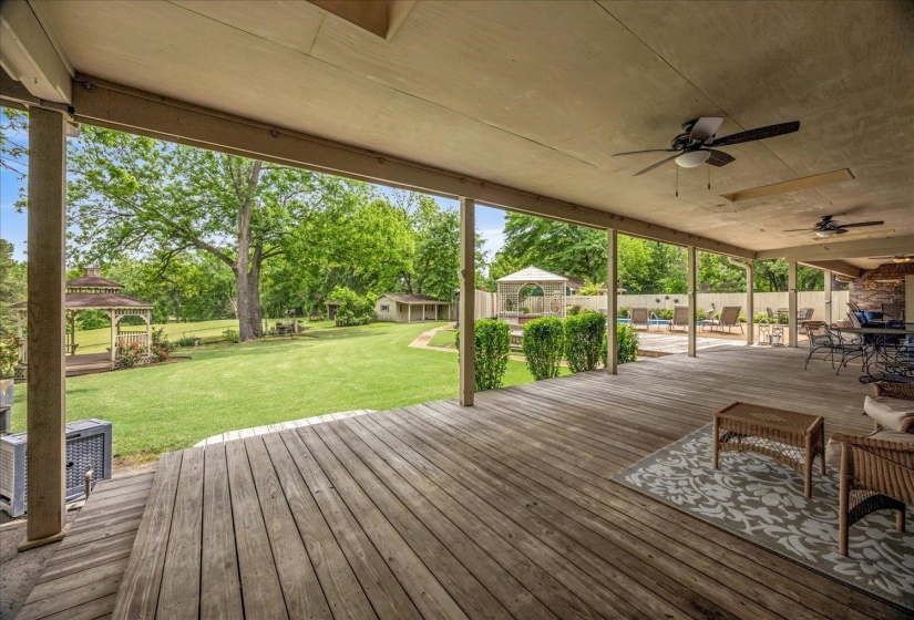 Expansive wood deck with an overhead cover, multiple ceiling fans, and views of the large lawn