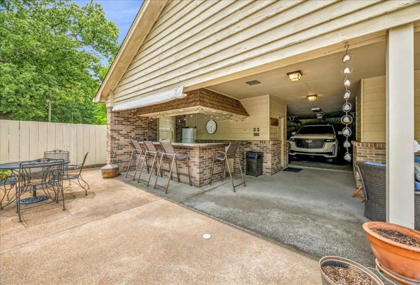 Outdoor bar with brick facade and serving window, integrated with a covered carport featuring recessed lighting