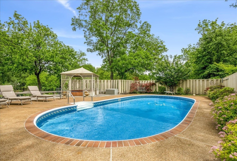 Oval-shaped in-ground pool with integrated steps, surrounded by a textured concrete deck and brick coping