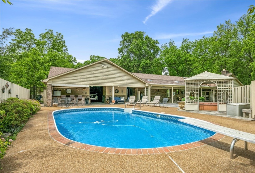 Outdoor swimming pool with a diving board, surrounded by exposed aggregate concrete decking and brick coping