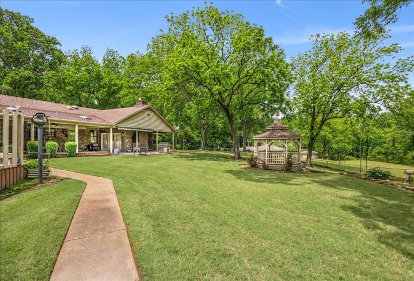 Expansive rear yard featuring a manicured lawn, established trees, and a decorative gazebo