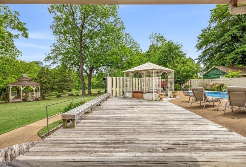 Expansive outdoor area featuring a wooden deck with built-in bench seating, an in-ground swimming pool, and a white lattice gazebo