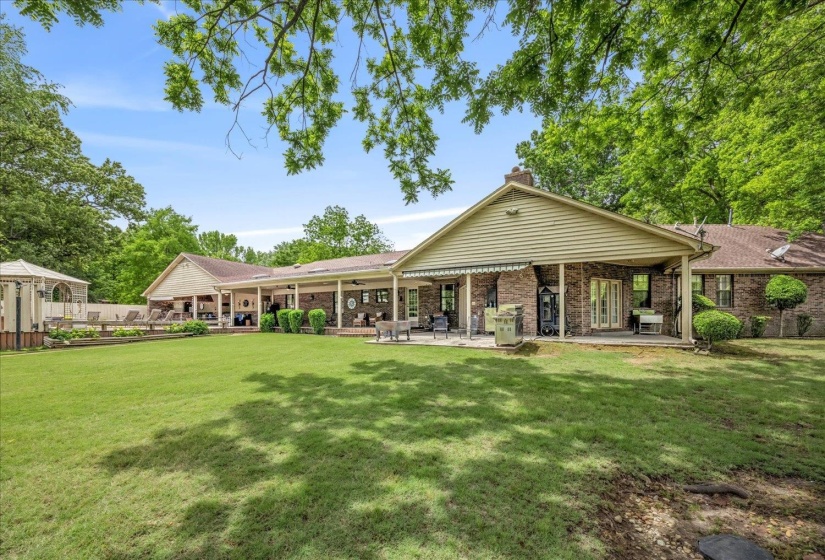 Expansive backyard featuring a manicured lawn, a large covered patio, brick exterior, and a detached gazebo structure