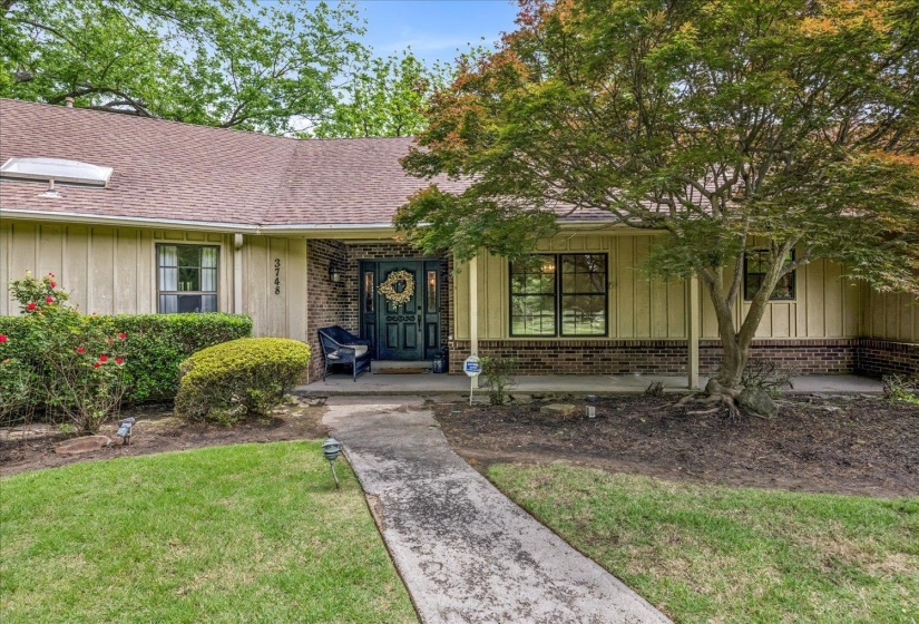 Front exterior featuring a dark paneled front door with sidelights, brick accents, vertical siding, a skylight, and a mature tree providing natural shade