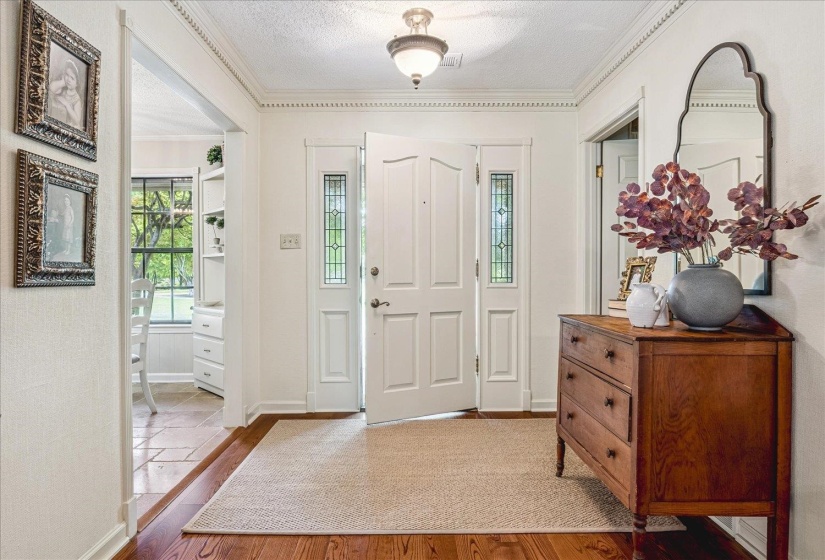 Front entry featuring a paneled door with decorative glass sidelights, polished wood-finish flooring, and crown molding