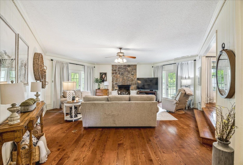 Living area featuring wood-finish flooring, a stone fireplace, crown molding, and two sets of French doors