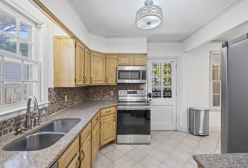 Kitchen featuring wood cabinetry, stainless steel appliances, speckled countertops, a mosaic tile backsplash, and light-toned tile flooring