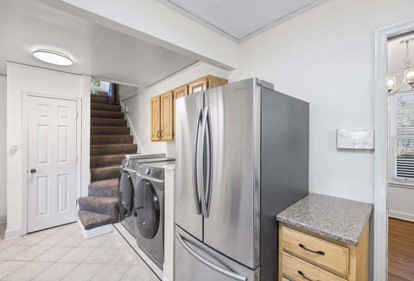 Laundry area featuring tiled flooring, a built-in staircase with carpet treads, and overhead cabinetry
