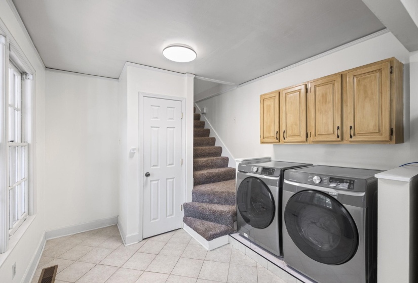 Laundry area featuring tile flooring, wood-finish cabinetry, a white paneled door, and carpeted stairs