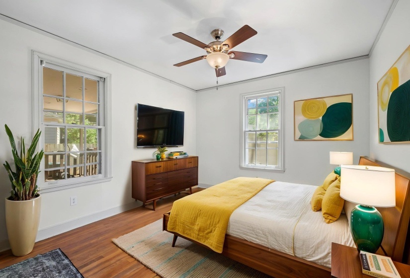 Hardwood-finish flooring featuring two large windows, a ceiling fan with light fixture, and crown molding