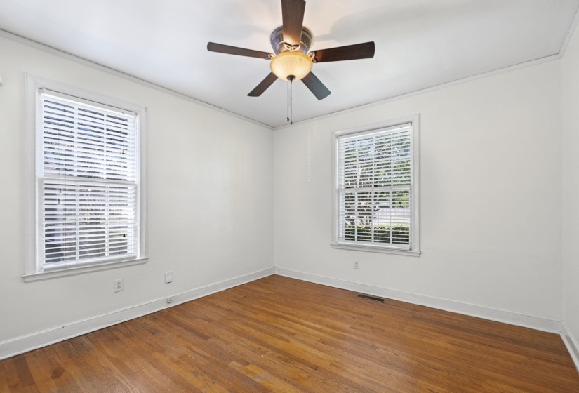 Bright room featuring two windows with white blinds, wood-finish flooring, a ceiling fan with integrated lighting, and white baseboards