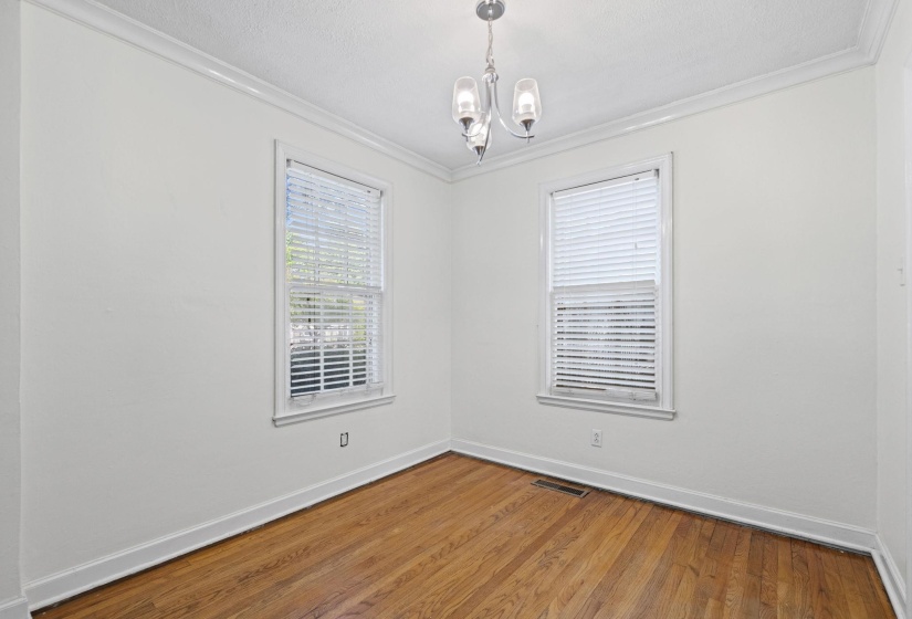 Interior space featuring wood-finish flooring, two windows with blinds, a ceiling-mounted light fixture, crown molding, and baseboards