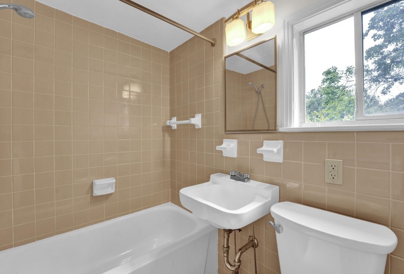 Bathroom featuring a white bathtub, wall-mounted sink, and toilet