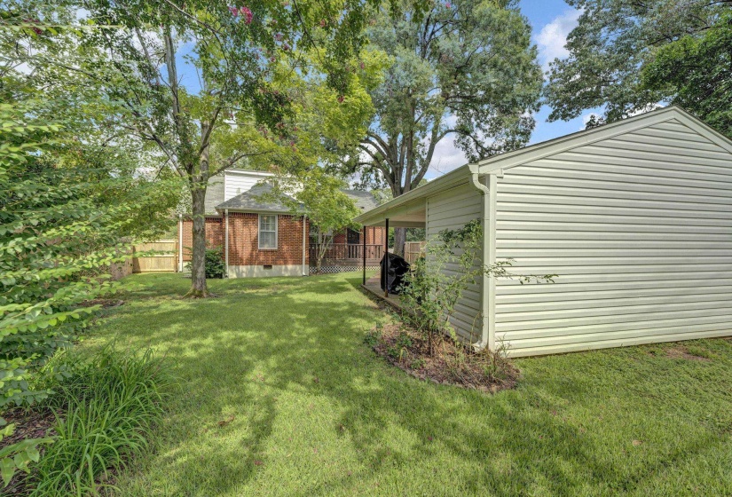 Expansive rear yard featuring manicured lawn, mature trees, and a detached structure with covered porch
