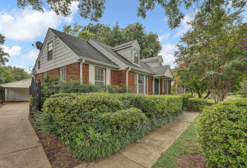 Brick and siding exterior featuring dormer windows, a covered front entry, and a paved driveway leading to a detached garage